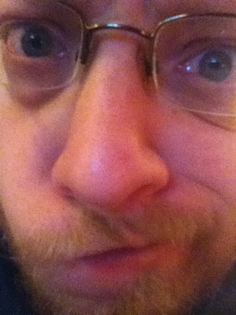 Four eyes, unkempt beard, big nose, smirk.